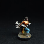 Une figurine du 7ème, La Traqueuse, vue de face, habillée de vêtement coloré jaune et orange, porte un filet dans ses mains.