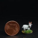 Une figurine du 7ème Continent à côté d’une pièce d’un centime d’euro, la Chèvre, une chèvre blanche dans une prairie entrain de brouter.