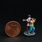 Une figurine du 7ème Continent à côté d’une pièce d’un centime d’euro, Philias Fogg et Jean Passepartout, deux personnages dos à dos, l’un grand, moustachu, habillé d’un costard rose et l’autre, petit et musclé, habillé de jaune.