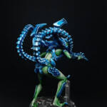 Intrus Adulte V2 Une figurine de Nemesis, Un Intrus adulte version 2, créature vue de derrière, bipède, possède deux bras et une queue, de couleur bleue pour les carapaces, se tient debout les bras en avant.