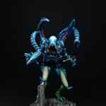 Intrus Adulte V2 Une figurine de Nemesis, Un Intrus adulte version 2, créature vue de face, bipède, possède deux bras et une queue, de couleur bleue pour les carapaces, se tient debout les bras en avant.