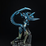 Intrus Adulte V1 Une figurine de Nemesis, Un Intrus adulte version 1, créature vue de derrière, bipède, possède deux bras et une queue, de couleur bleue pour les carapaces, se tient debout et prend appui sur un débris de fer.