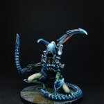 Une figurine de Nemesis, Un Intrus adulte version 3, créature vue de face, bipède, possède deux bras et une queue, de couleur bleue pour les carapaces, se tient accroupie.