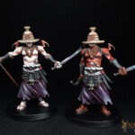 Hanyo-Shiro et Hanyo-Aka Duo de figurines d’Okko Chronicles, Hanyo-Shiro et Hanyo-Aka, personnage démonique vue de face, l’un de couleur blanche, l’autre rouge, le visage caché par un chapeau de paille et chacun équipé de deux armes.