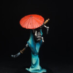 Oni-Miroyoku Une figurine d’Okko Chronicles, Oni-Miroyoku, personnage vue de derrière, grande femme au visage démoniaque et blanc, vêtue d’une robe bleue, porte une ombrelle et une arme dans l’autre main.