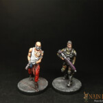 Le Prisonnier et le Chasseur de primes Duo de figurines de Nemesis, Le Chasseur de primes et le Prisonnier, personnage vue de face, barbu et armé pour l’un, vêtu d’un débardeur blanc et qui porte une muselière pour l’autre.