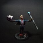 Personnage avec les bras grand ouvert sur les côtés et se tirant vers le ciel. Dans une main un grimoire, dans l'autre un bâton.